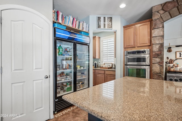kitchen featuring light brown cabinetry, light stone counters, tile patterned flooring, double oven, and built in refrigerator