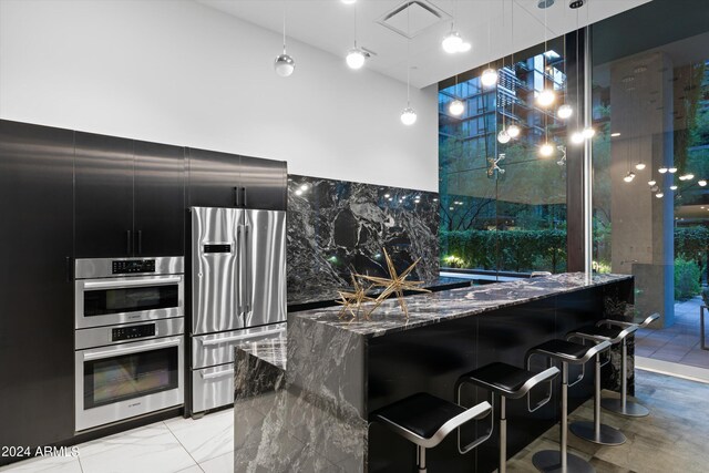 kitchen with a kitchen bar, appliances with stainless steel finishes, dark stone countertops, and pendant lighting