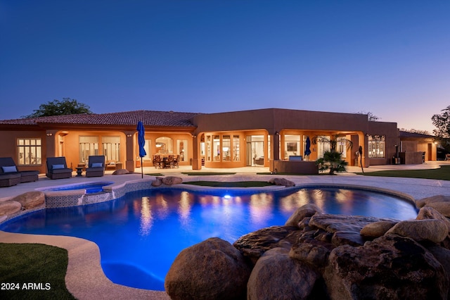 pool at dusk with an in ground hot tub and a patio area