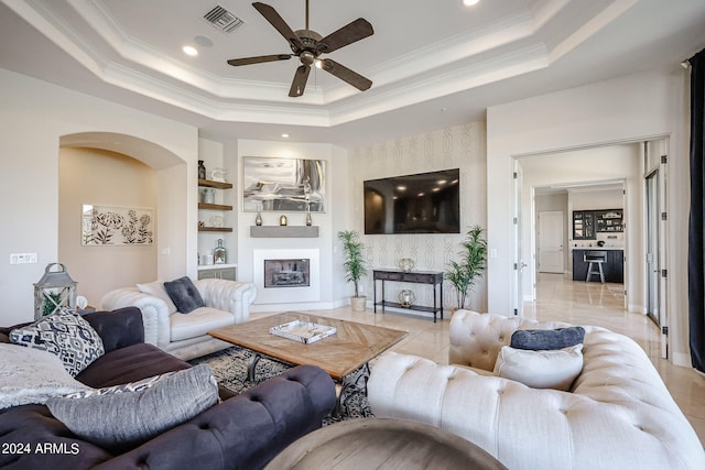 living room featuring built in shelves, a raised ceiling, ceiling fan, and a large fireplace