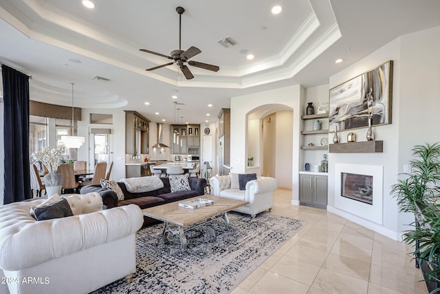 living room with ornamental molding, ceiling fan, a raised ceiling, and light tile patterned flooring