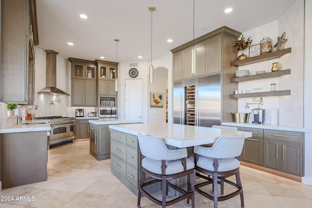 kitchen featuring a breakfast bar, pendant lighting, a center island, high end appliances, and wall chimney exhaust hood