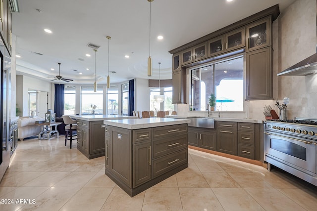 kitchen featuring ceiling fan, hanging light fixtures, sink, wall chimney range hood, and a center island