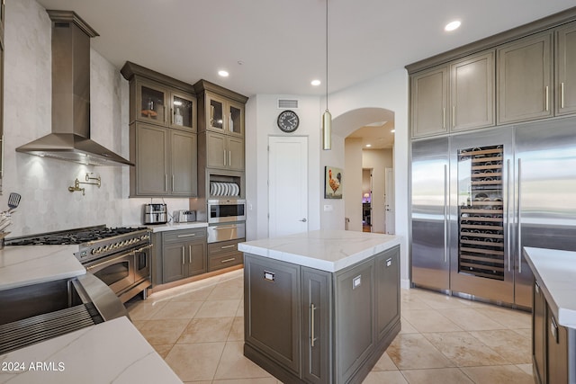 kitchen featuring light stone counters, pendant lighting, high end appliances, a kitchen island, and wall chimney exhaust hood