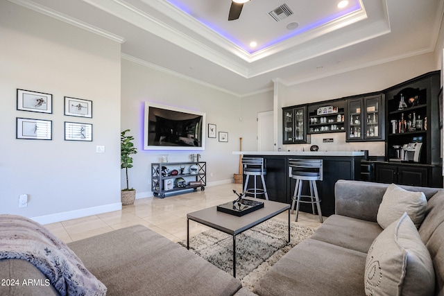 tiled living room featuring ornamental molding, a tray ceiling, ceiling fan, and bar area