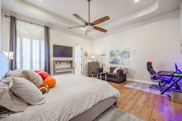 bedroom with wood-type flooring, ceiling fan, and a raised ceiling