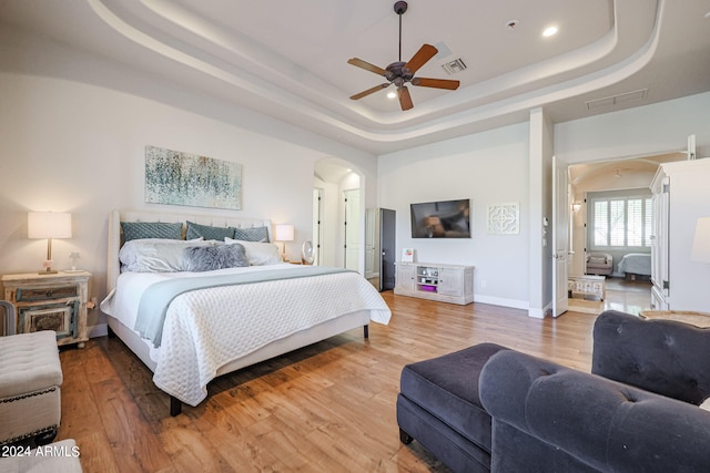 bedroom with wood-type flooring, ceiling fan, and a raised ceiling