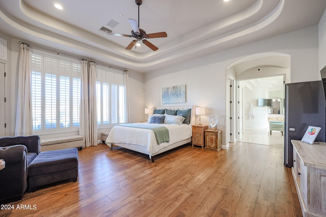 bedroom featuring ceiling fan, a tray ceiling, and light hardwood / wood-style flooring