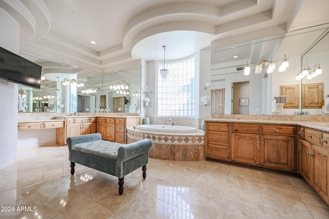 bathroom featuring vanity, a tray ceiling, a chandelier, and a relaxing tiled tub