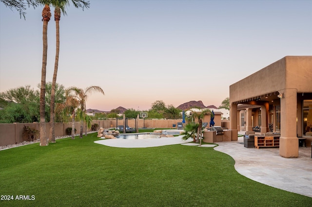 yard at dusk featuring an outdoor kitchen and a patio area