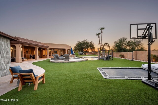 yard at dusk featuring a patio, a trampoline, and an outdoor hangout area