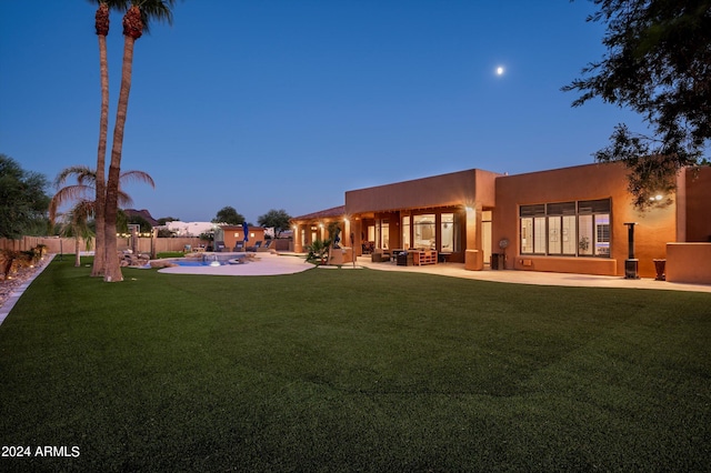 back house at dusk with a lawn and a patio area