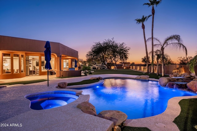 pool at dusk with a patio, an in ground hot tub, and pool water feature