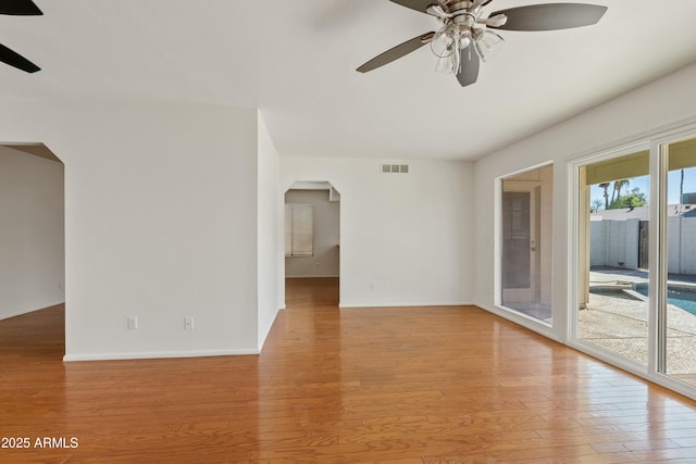 empty room with baseboards, light wood-style floors, visible vents, ceiling fan, and arched walkways