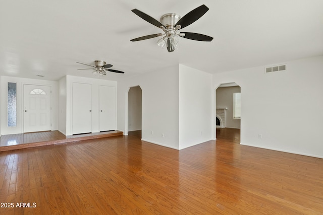unfurnished living room featuring baseboards, a ceiling fan, visible vents, arched walkways, and light wood finished floors