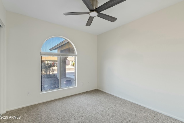 carpeted spare room featuring baseboards and a ceiling fan