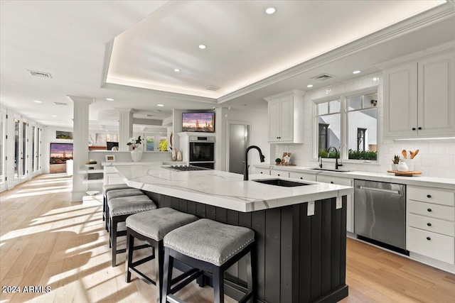 kitchen with light hardwood / wood-style flooring, a kitchen island, tasteful backsplash, a tray ceiling, and stainless steel appliances