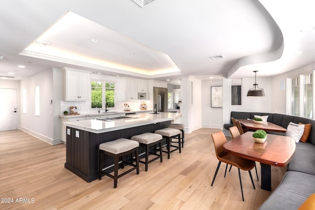 kitchen featuring light wood-type flooring, a kitchen breakfast bar, a tray ceiling, a large island, and white cabinetry