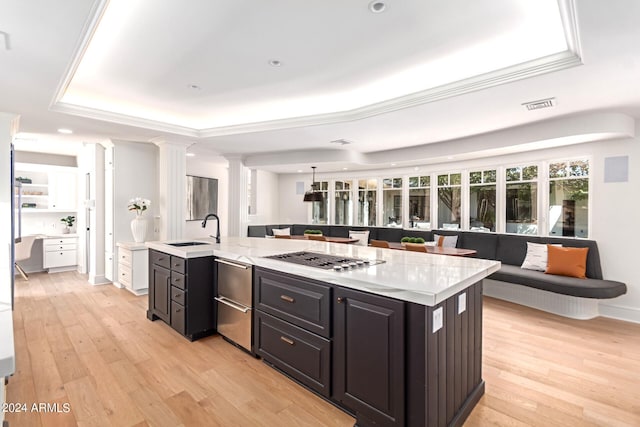 kitchen featuring light hardwood / wood-style flooring, sink, an island with sink, stainless steel gas stovetop, and a tray ceiling