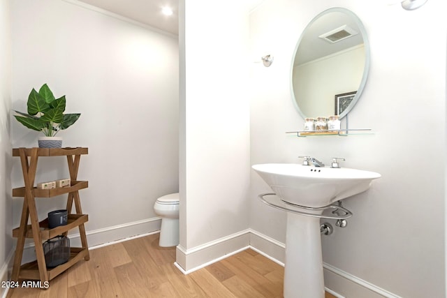 bathroom with toilet, hardwood / wood-style floors, and ornamental molding