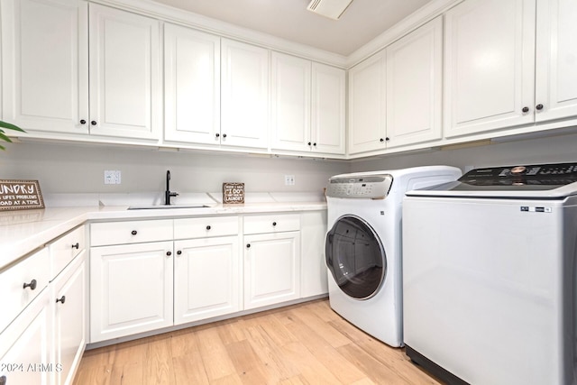 laundry room featuring sink, washer and clothes dryer, light hardwood / wood-style floors, and cabinets