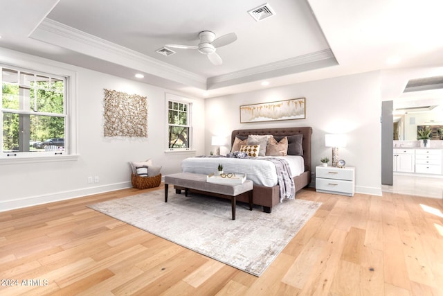 bedroom featuring ornamental molding, ensuite bath, light hardwood / wood-style floors, ceiling fan, and a raised ceiling