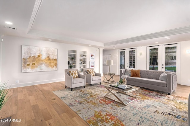 living room with built in features, french doors, light hardwood / wood-style floors, and a tray ceiling