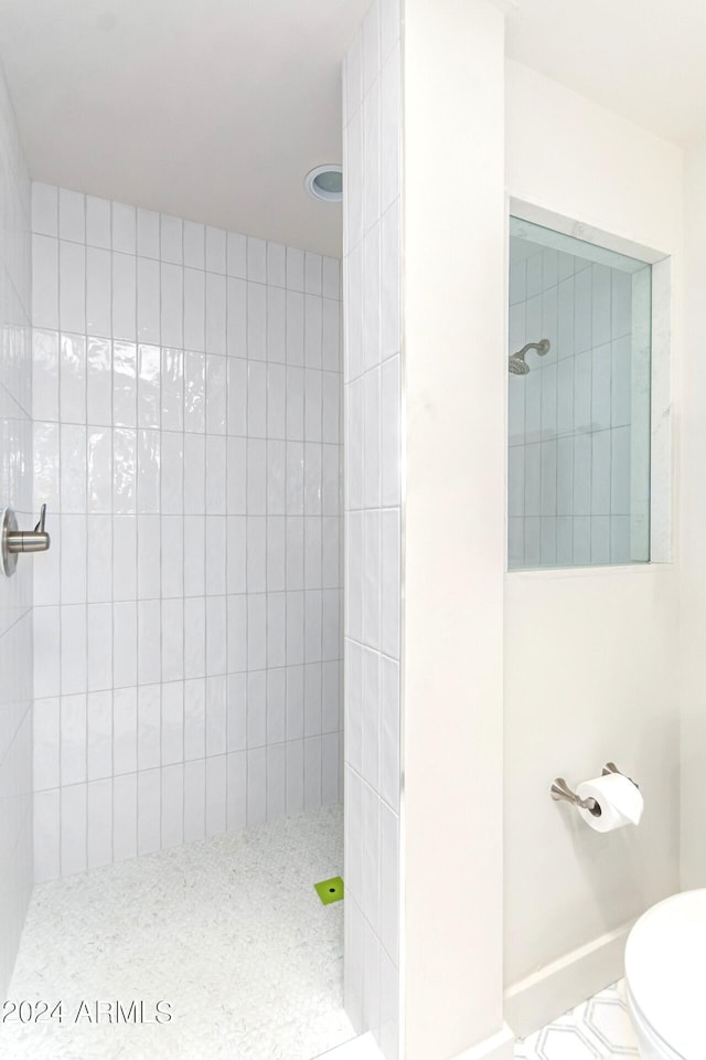 bathroom featuring toilet, a tile shower, and tile patterned floors