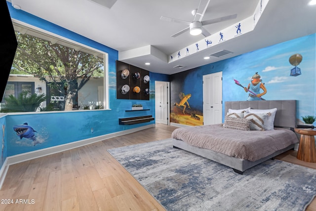 bedroom with hardwood / wood-style flooring, a raised ceiling, and ceiling fan