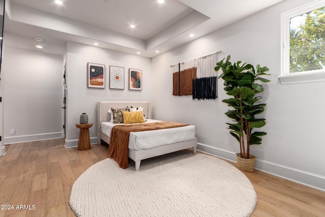 bedroom with a tray ceiling and light wood-type flooring