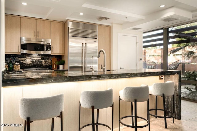 kitchen with sink, appliances with stainless steel finishes, a kitchen bar, dark stone counters, and light brown cabinets