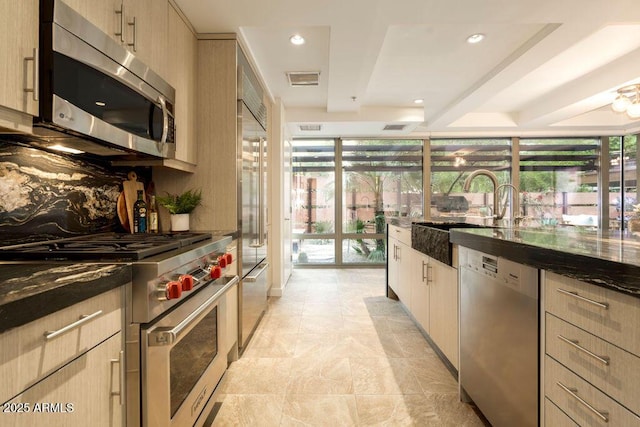 kitchen featuring dark stone countertops, light brown cabinetry, and appliances with stainless steel finishes