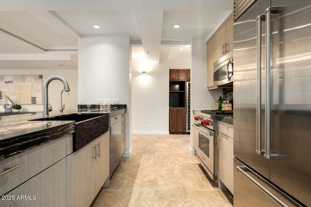 kitchen featuring high end appliances, sink, and dark stone countertops