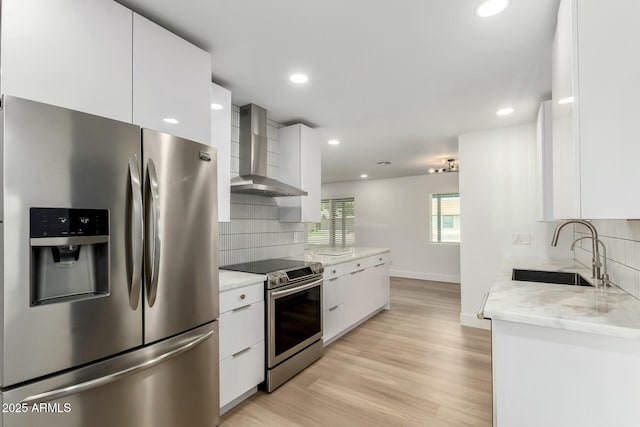 kitchen with modern cabinets, tasteful backsplash, wall chimney range hood, a sink, and stainless steel appliances