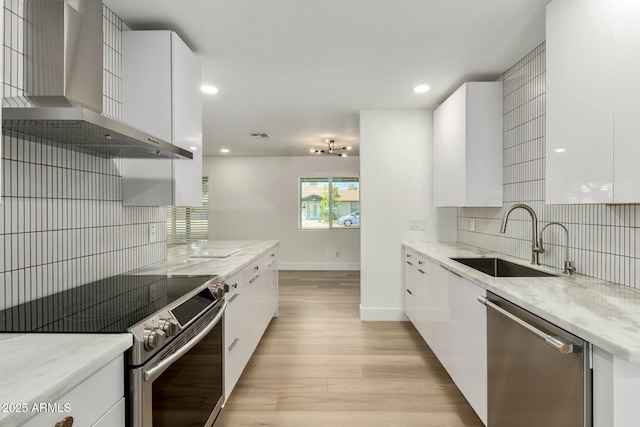 kitchen featuring a sink, wall chimney range hood, appliances with stainless steel finishes, and modern cabinets