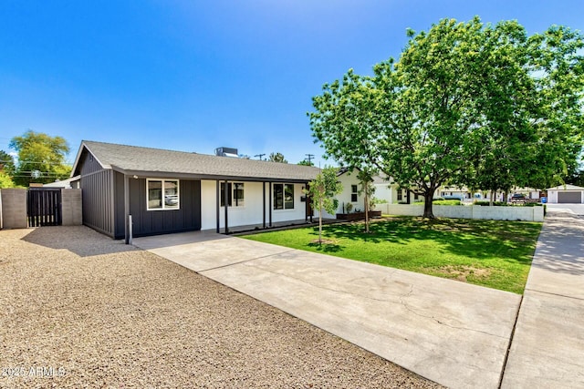 ranch-style house featuring driveway, board and batten siding, fence, and a front lawn