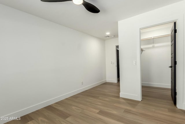 unfurnished bedroom with baseboards, a closet, a spacious closet, ceiling fan, and wood finished floors