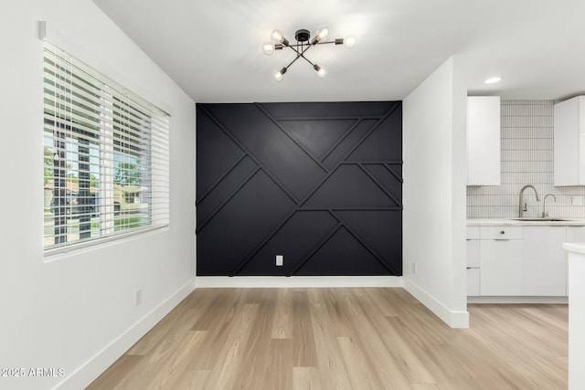 unfurnished dining area featuring a chandelier, light wood-style floors, baseboards, and a sink