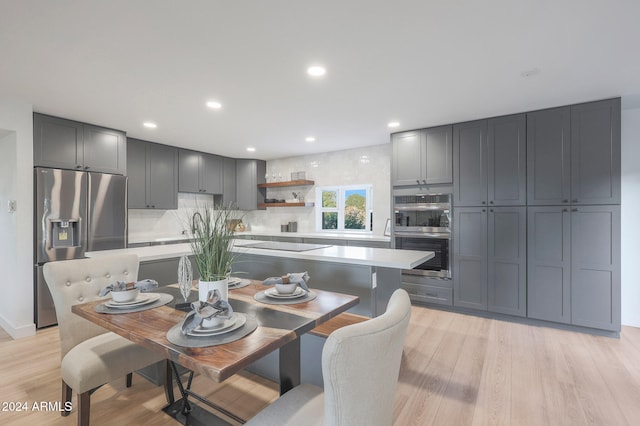 kitchen featuring light hardwood / wood-style floors, decorative backsplash, gray cabinetry, a kitchen island, and appliances with stainless steel finishes