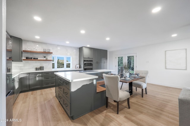 kitchen with gray cabinetry, a kitchen island, decorative backsplash, light hardwood / wood-style floors, and double oven