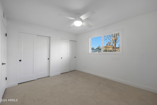 unfurnished bedroom featuring light colored carpet, ceiling fan, and two closets