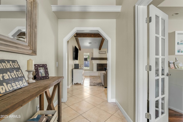 hallway with baseboards, arched walkways, beamed ceiling, and light tile patterned flooring