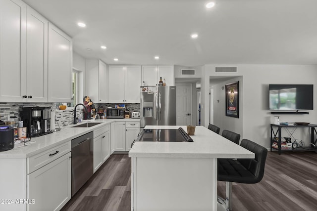 kitchen with appliances with stainless steel finishes, dark hardwood / wood-style flooring, white cabinets, a center island, and a breakfast bar area