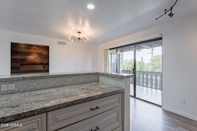 kitchen featuring a chandelier, dark stone counters, wood finished floors, baseboards, and white cabinets