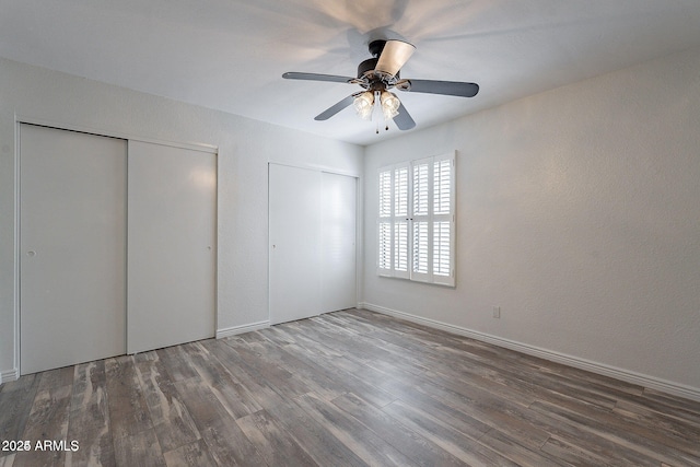 unfurnished bedroom featuring multiple closets, wood finished floors, and ceiling fan