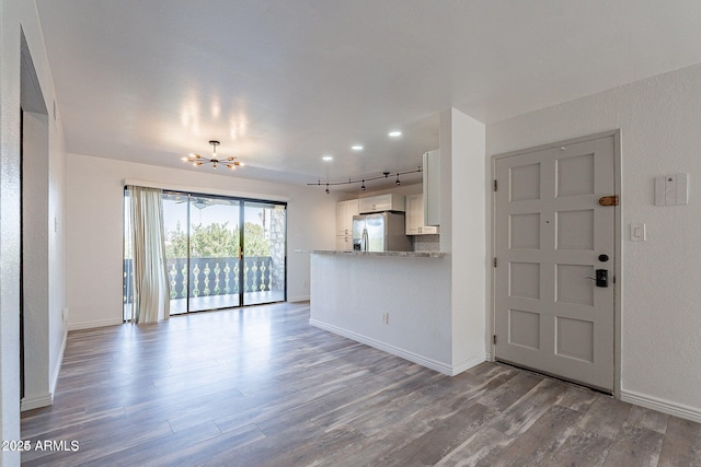 unfurnished living room featuring wood finished floors, a chandelier, rail lighting, and baseboards