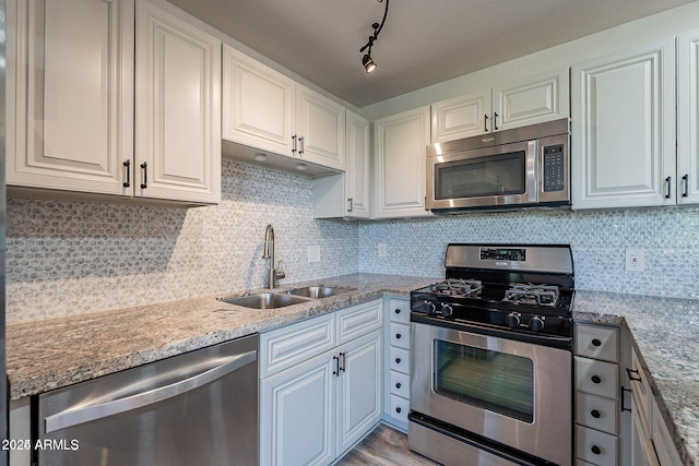 kitchen featuring stainless steel appliances, a sink, white cabinets, light stone countertops, and light wood-type flooring