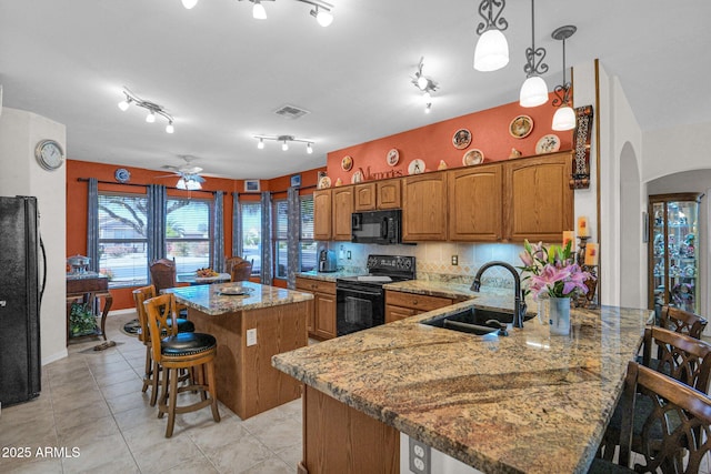 kitchen featuring decorative light fixtures, a center island, black appliances, a kitchen bar, and sink