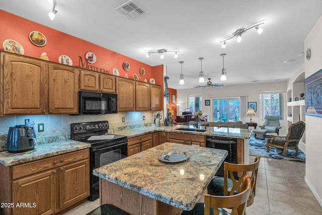 kitchen featuring kitchen peninsula, a breakfast bar area, decorative light fixtures, black appliances, and a center island