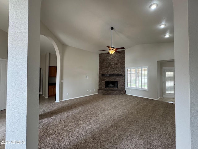unfurnished living room featuring baseboards, a fireplace, arched walkways, ceiling fan, and carpet flooring